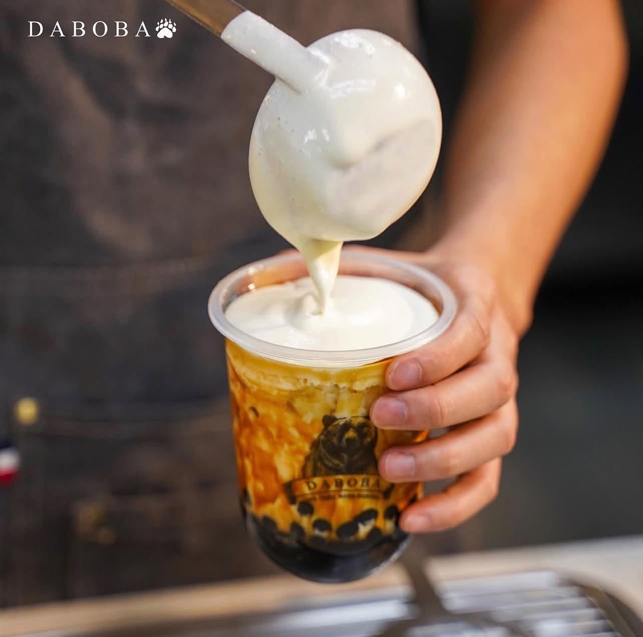 A scoop of creamy milk foam being poured over a brown sugar boba milk tea at Daboba